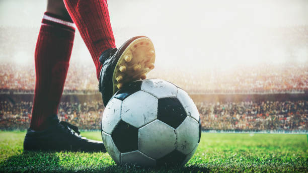 Pied de footballer sur un ballon, sur la pelouse d'un stade